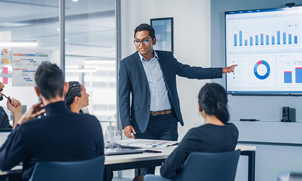A board meeting presentation with a display of graphs