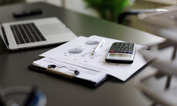 An image of a desk with paper, calculator and a laptop on it
